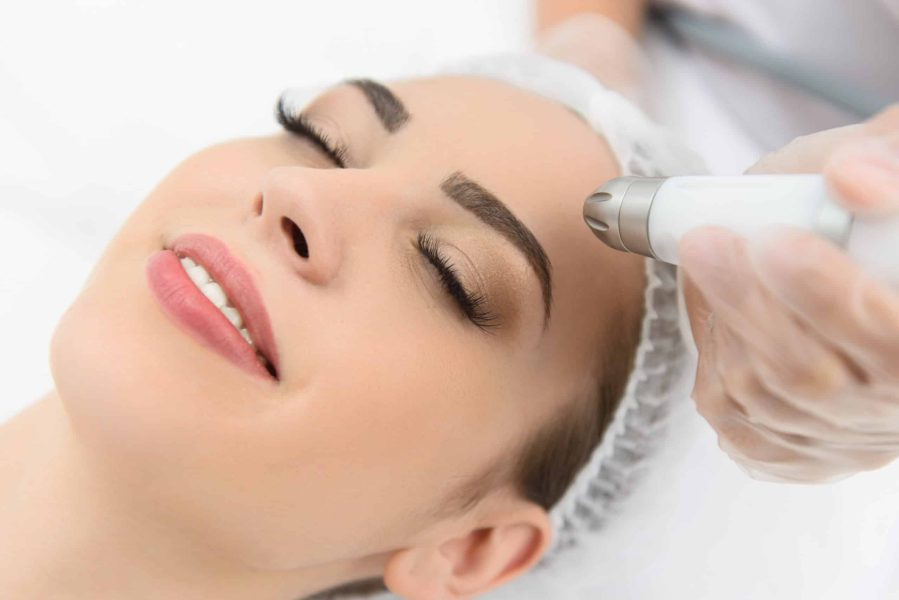 Close up of young girl having stimulating facial treatment at professional clinic. She is smiling with closed eyes